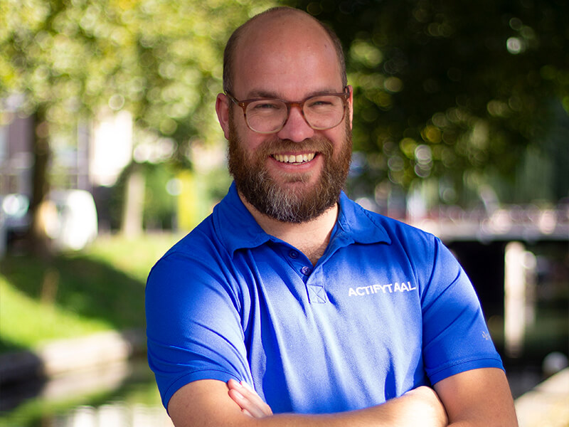 Manueel therapeut Hidde Heineman poseert voor zijn profielfoto in een blauw shirt en lacht naar de camera.