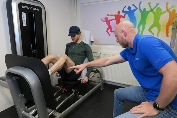 Man sport in de oefenzaal na het oplopen van beenblessures en wordt geholpen door fysiotherapeit siko van actifytaal