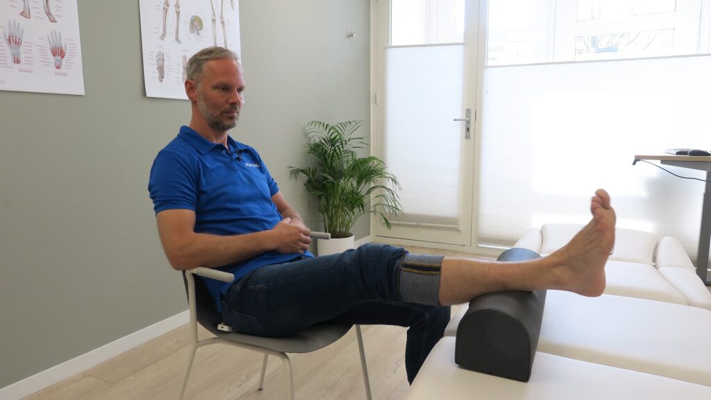 Patiënt met blauw shirt zit met scheenbeenklachten in de behandelkamer