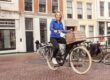 Vrolijke vrouw fietst door de stad met houten krat op fiets.