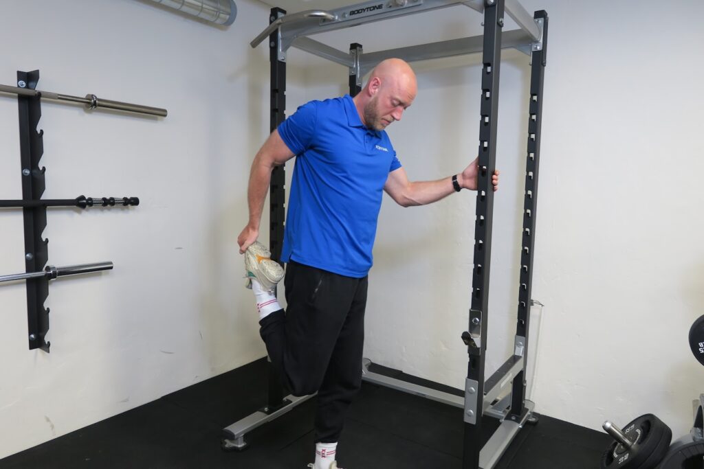 Man in blauw shirt doet beenstrek oefening in sportschool