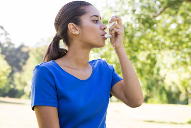Vrouw met Astma in een blauw shirt is buiten aanwezig en gebruikt een puffer voor haar ademhaling