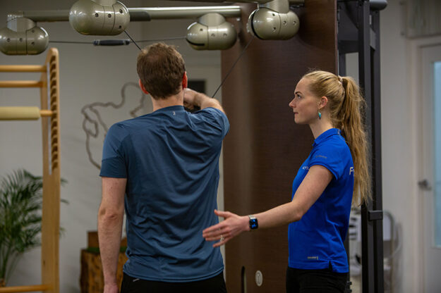Man wilt stress en rugklachten voorkomen door middel van fysiotherapie samen met de fysiotherapeut in een blauw shirt.