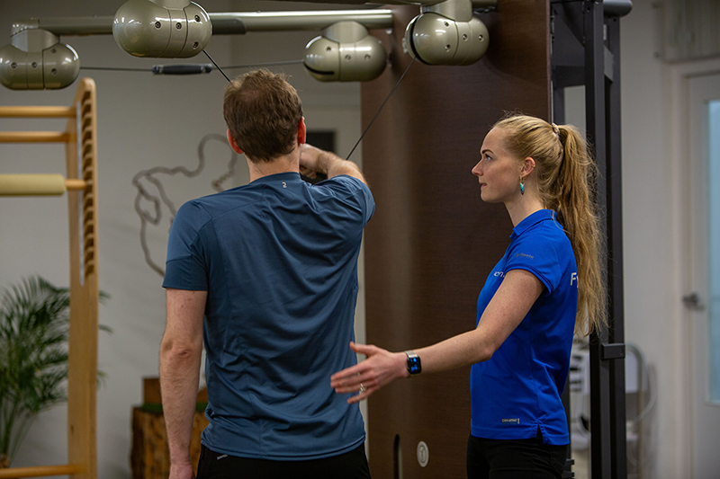 Man wilt stress en rugklachten voorkomen door middel van fysiotherapie samen met de fysiotherapeut in een blauw shirt.
