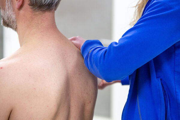 hernia Patiënt met een hernia wordt geholpen aan omliggende klachten door de fysiotherapeut in een blauw shirt