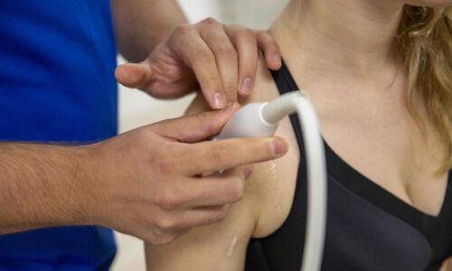 Fysiotherapeut voert een schouderbehandeling uit met echografie, waarbij de schouder van een patiënt nauwkeurig wordt onderzocht.