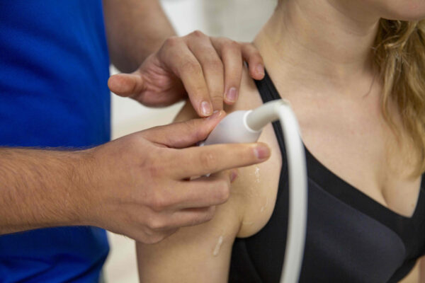 Fysiotherapeut voert een schouderbehandeling uit met echografie, waarbij de schouder van een patiënt nauwkeurig wordt onderzocht.