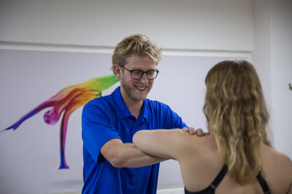 tennisarm Vrouwelijke patiënt met een tennisarm wordt geholpen door een fysiotherapeut in een blauw shirt met een bril in de behandelkamer