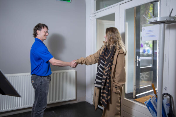 Fysiotherapeut schudt een patiënt de hand bij binnenkomst in de praktijk, als welkom en eerste contactmoment.
