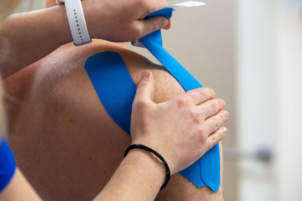 Close-up van medical taping op de schouder van een patiënt met blauwe tape in de behandelkamer.
