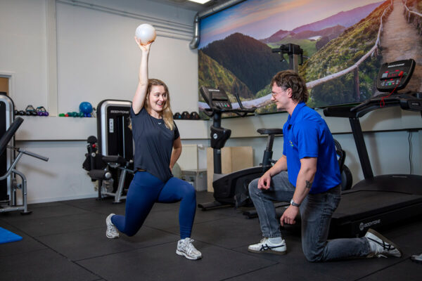 personal training Vrouwelijke patiënt kijgt personal training van de fysiotherapeut in de oefenzaal en doet oefeningen met een bal