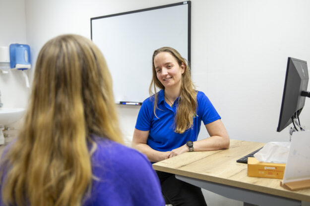 Vrouw met lang bruin haar is in gesprek met de fysio over haar klachten bij een burn-out.